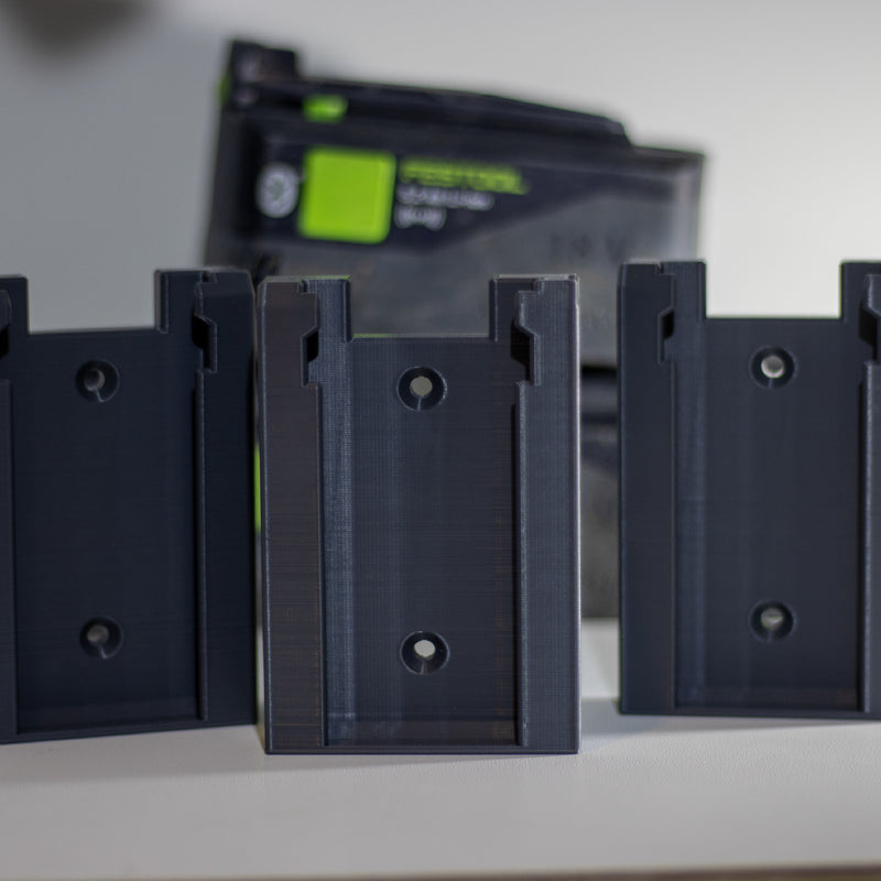 Drie Festool accuhouders op een rij met een Festool accu op de achtergrond