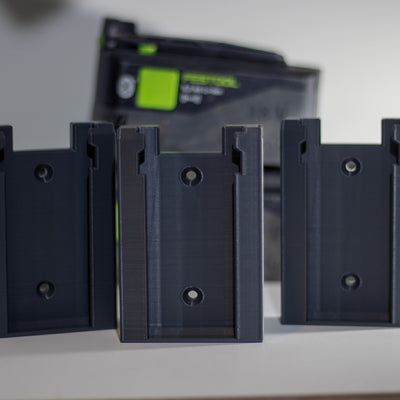 Drie Festool accuhouders op een rij met een Festool accu op de achtergrond
