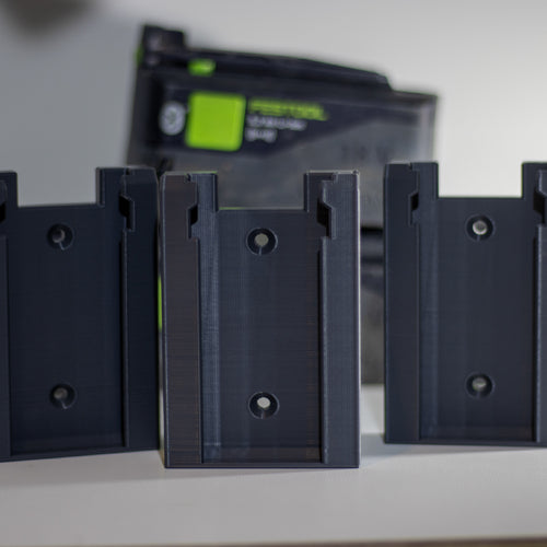 Drie Festool accuhouders op een rij met een Festool accu op de achtergrond