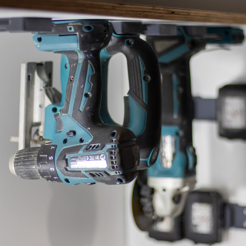 Makita machines hangen ondersteboven in gereedschaphouders onder een plank